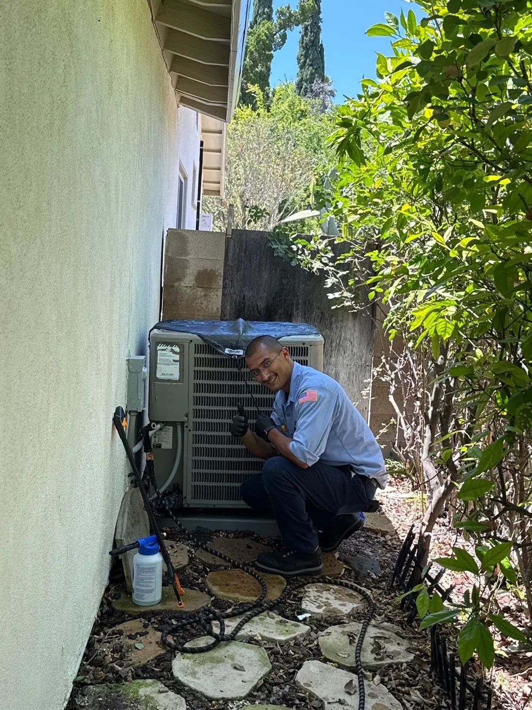 AirtekPros technician kneeling beside a residential outdoor condensing unit during a service call