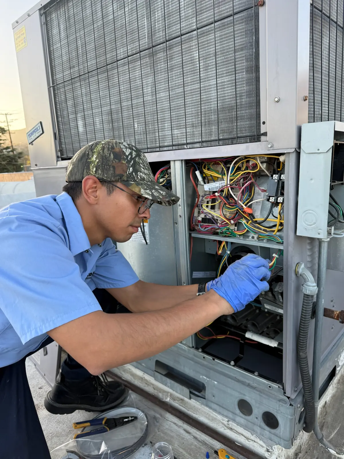 AirtekPros technician working inside an open package unit control compartment with the wiring exposed