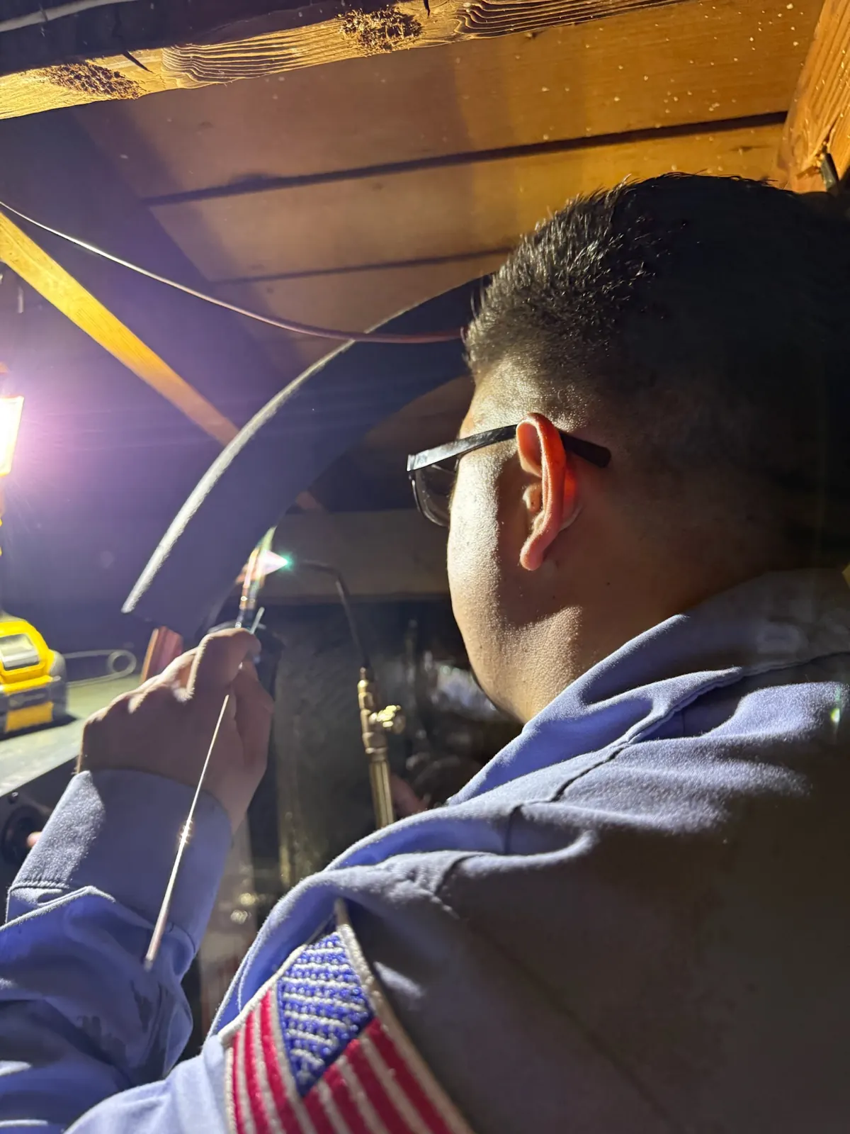 AirtekPros technician brazing a copper refrigerant line joint with a torch while wearing safety glasses