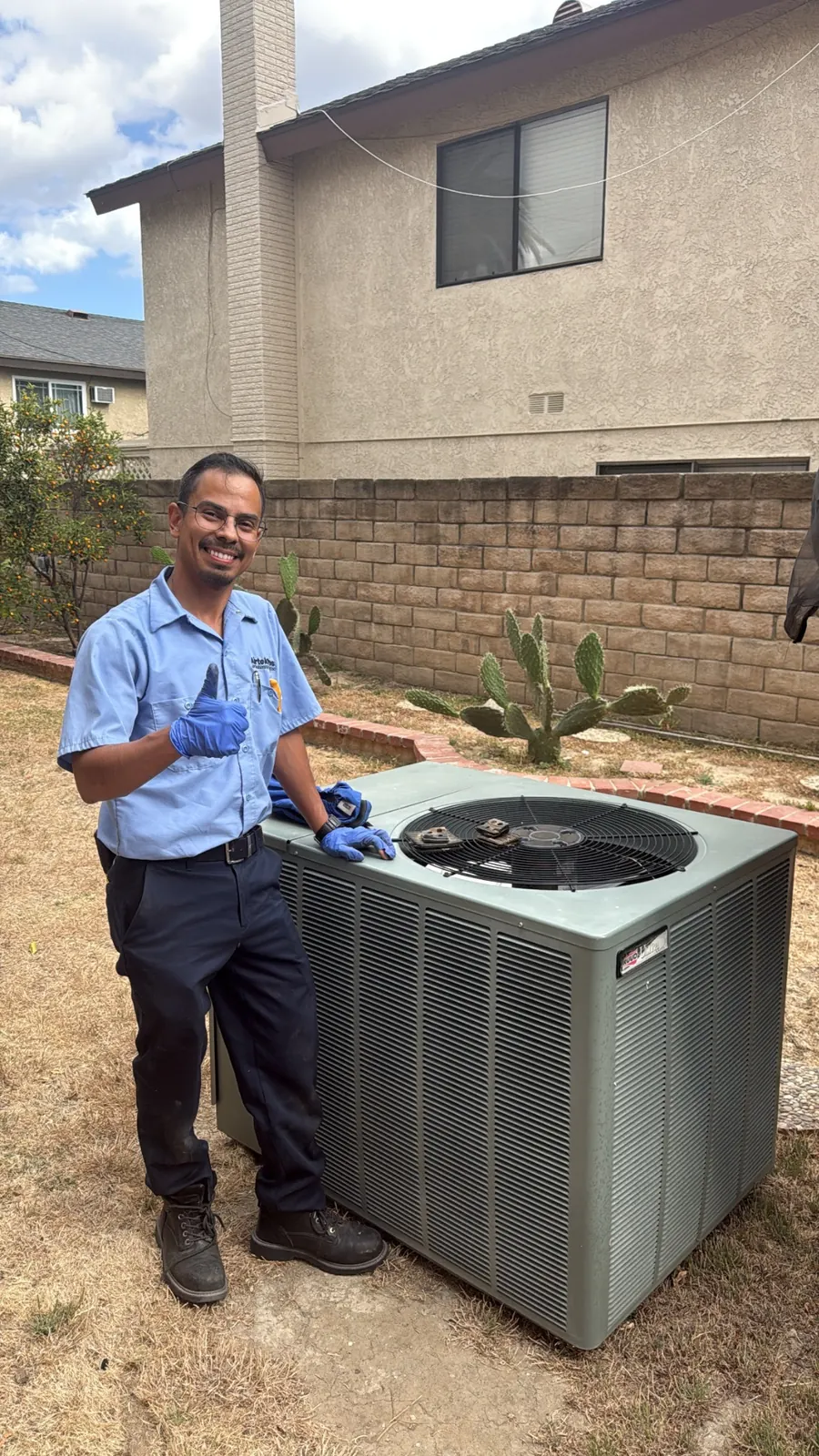 Smiling AirtekPros technician in uniform standing beside a residential outdoor condensing unit after a service call