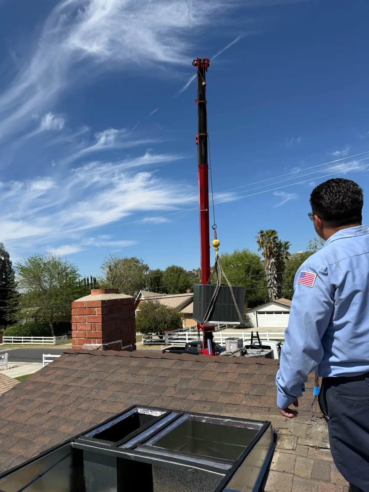 Crane lifting an HVAC unit over a house roof during an AirtekPros system replacement