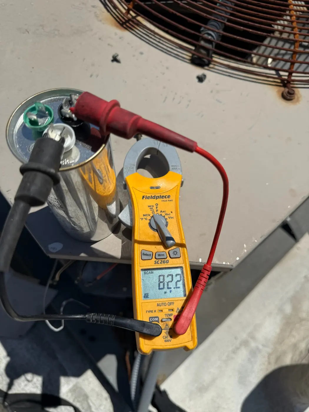 Multimeter leads on a run capacitor at an outdoor unit showing a live measurement