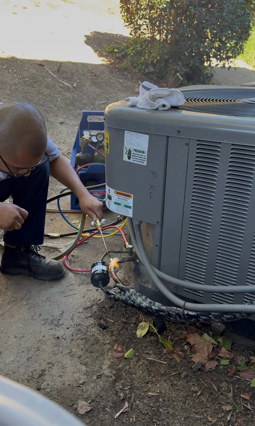 AirtekPros technician connecting service hoses to an outdoor condensing unit in a side yard