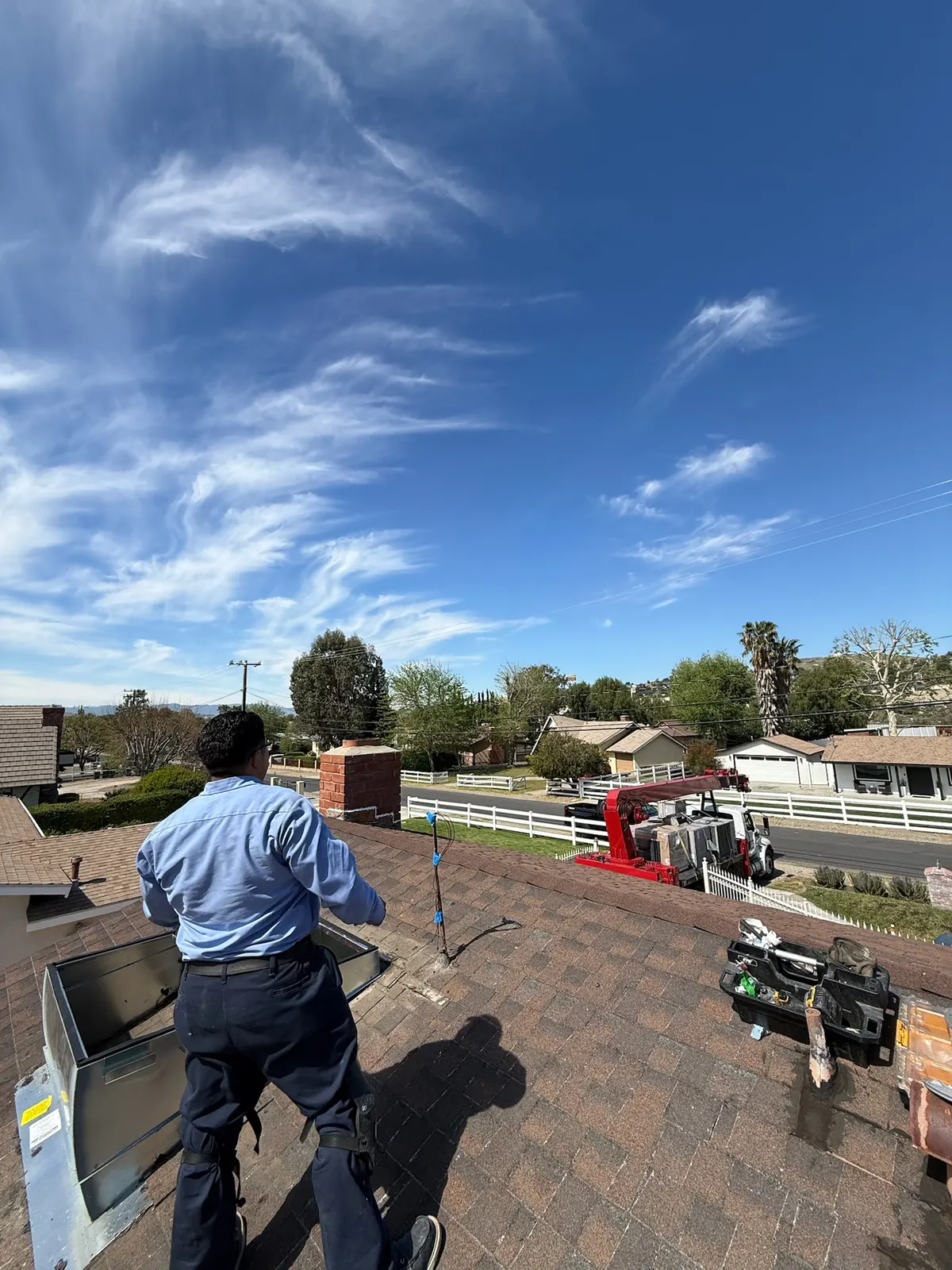 AirtekPros technician on a residential roof beside HVAC equipment under a clear sky