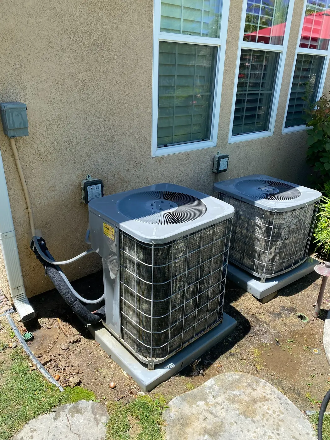 Two newly installed residential condensing units set on pads alongside a home