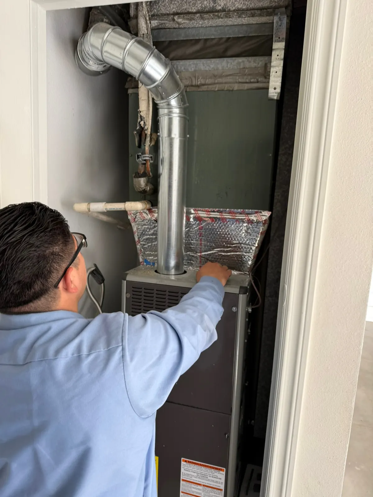 AirtekPros technician checking the flue and cabinet of a furnace in an indoor utility closet