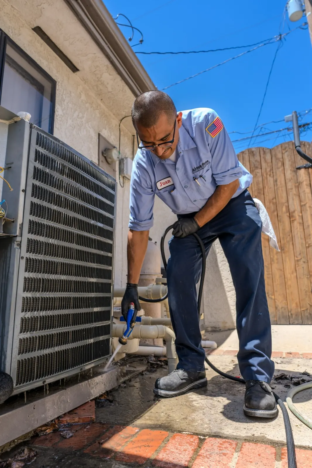 AirtekPros technician rinsing the coil of an outdoor condensing unit during a maintenance visit