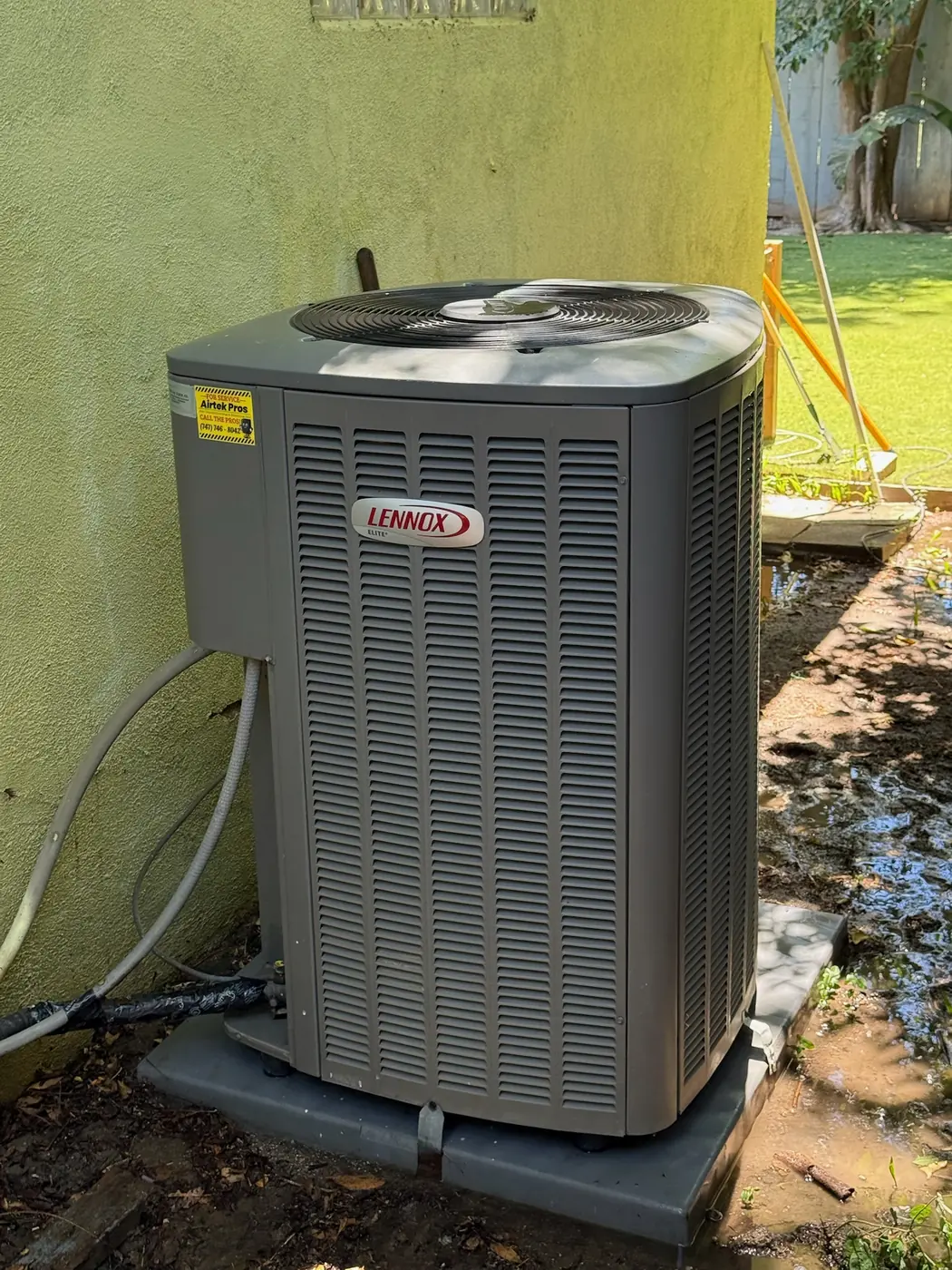 Newly installed Lennox condensing unit set on a pad beside a stucco wall