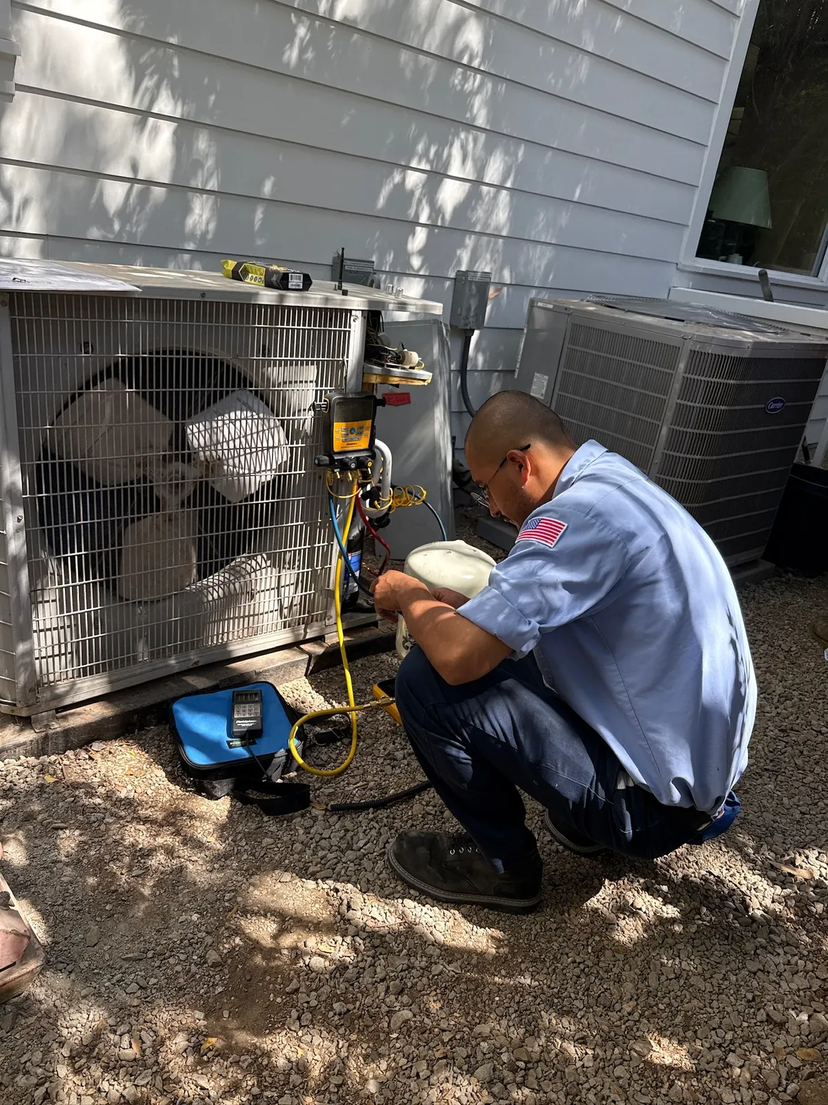 AirtekPros technician kneeling at an outdoor AC condenser with refrigerant gauges connected to the service ports