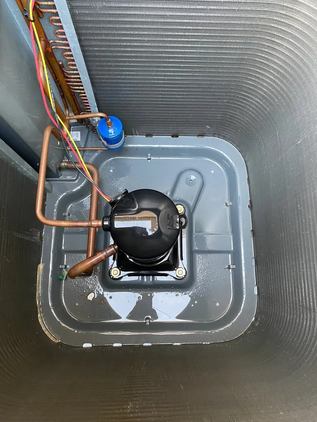 Top-down view inside an outdoor condensing unit showing the compressor and refrigerant lines