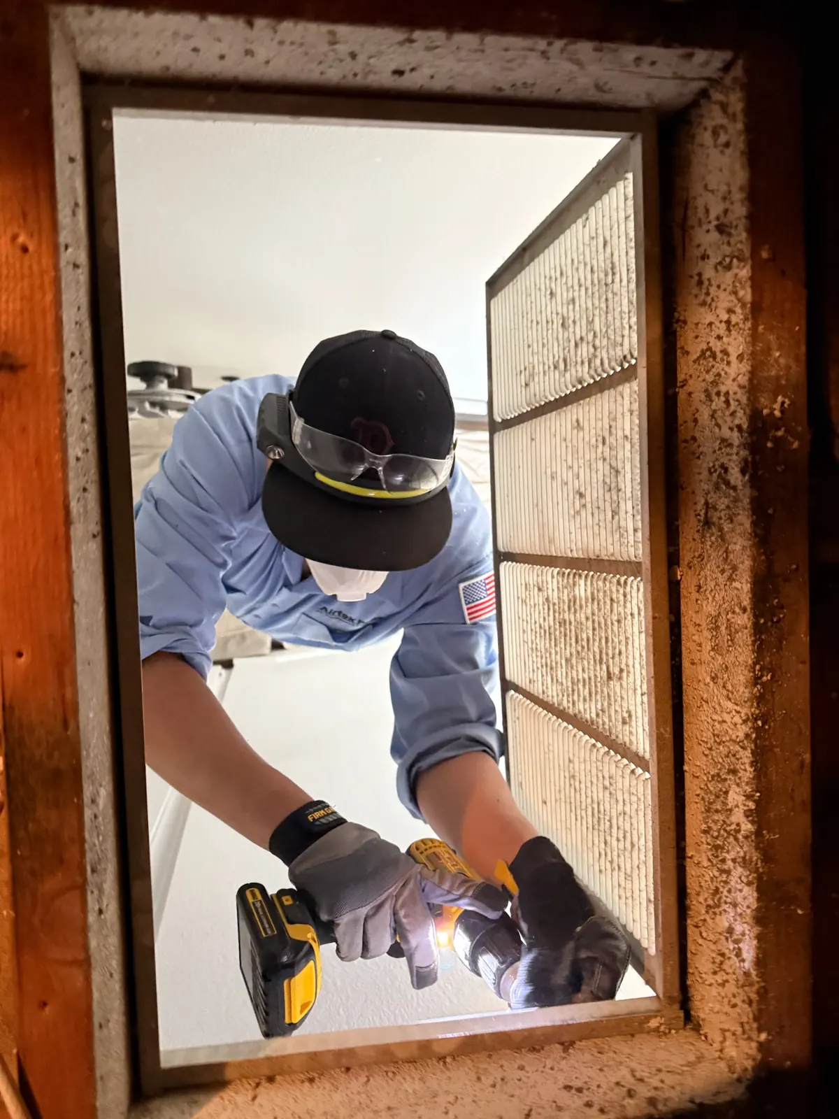AirtekPros technician inspecting and cleaning a dirty return duct opening with a work light