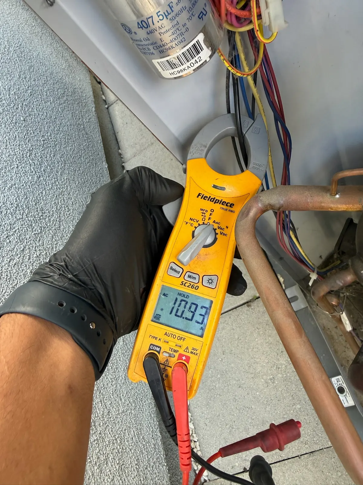 Clamp meter showing a live voltage reading on the wiring of an outdoor HVAC disconnect